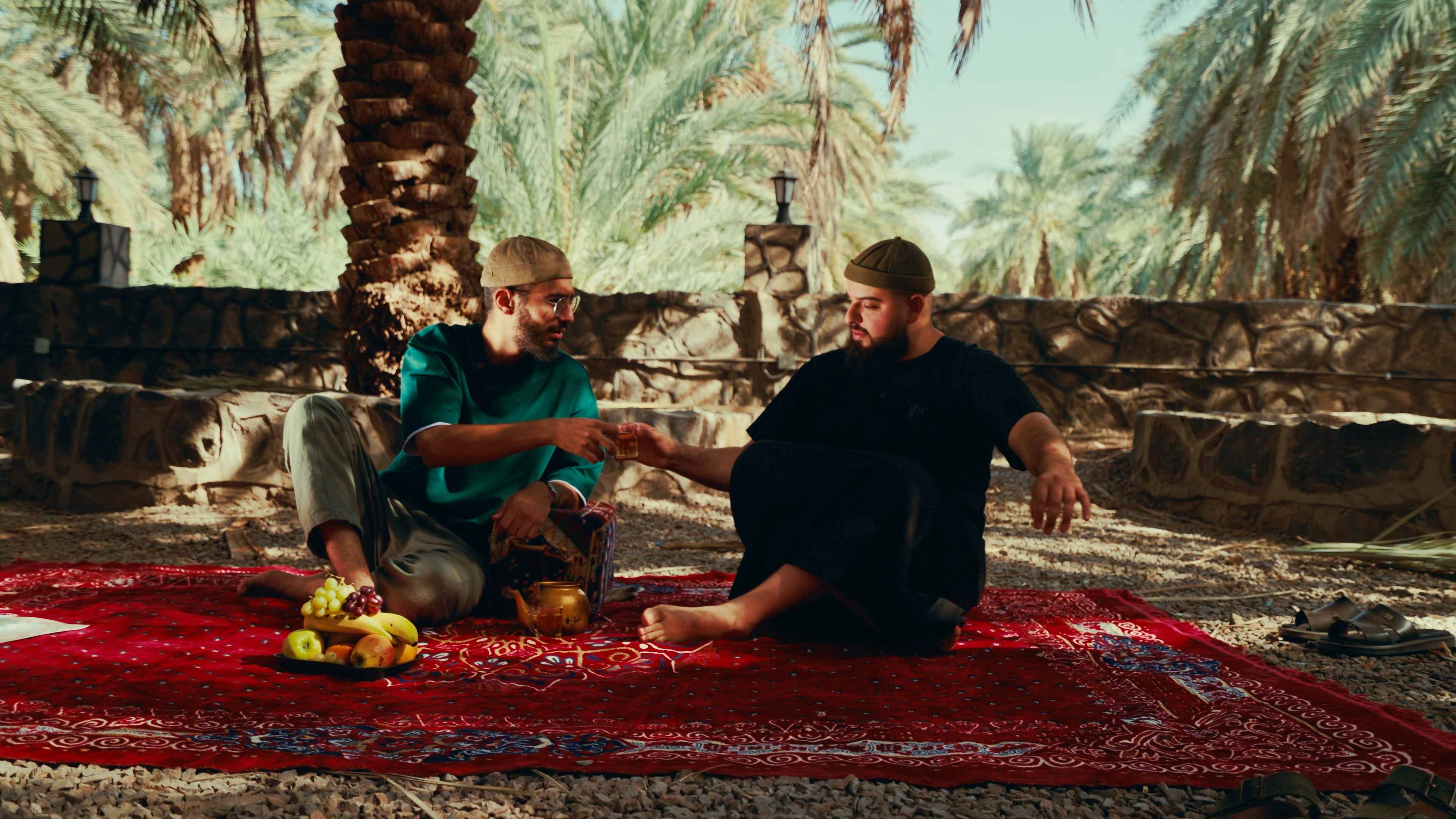 The crew sharing tea on a rug beneath the palms between shoots